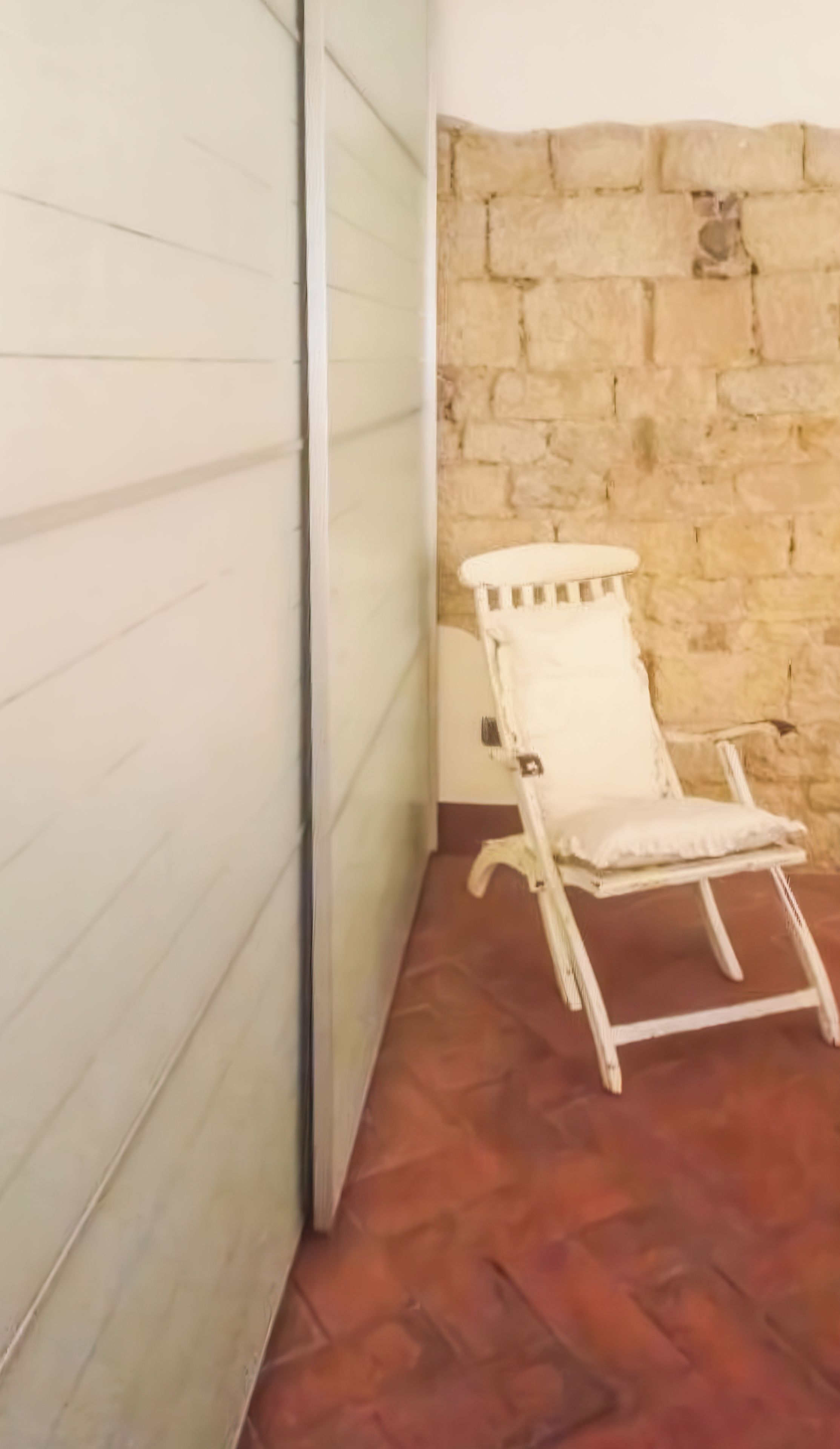 A room with a stone wall, a white chair, and a patterned floor.