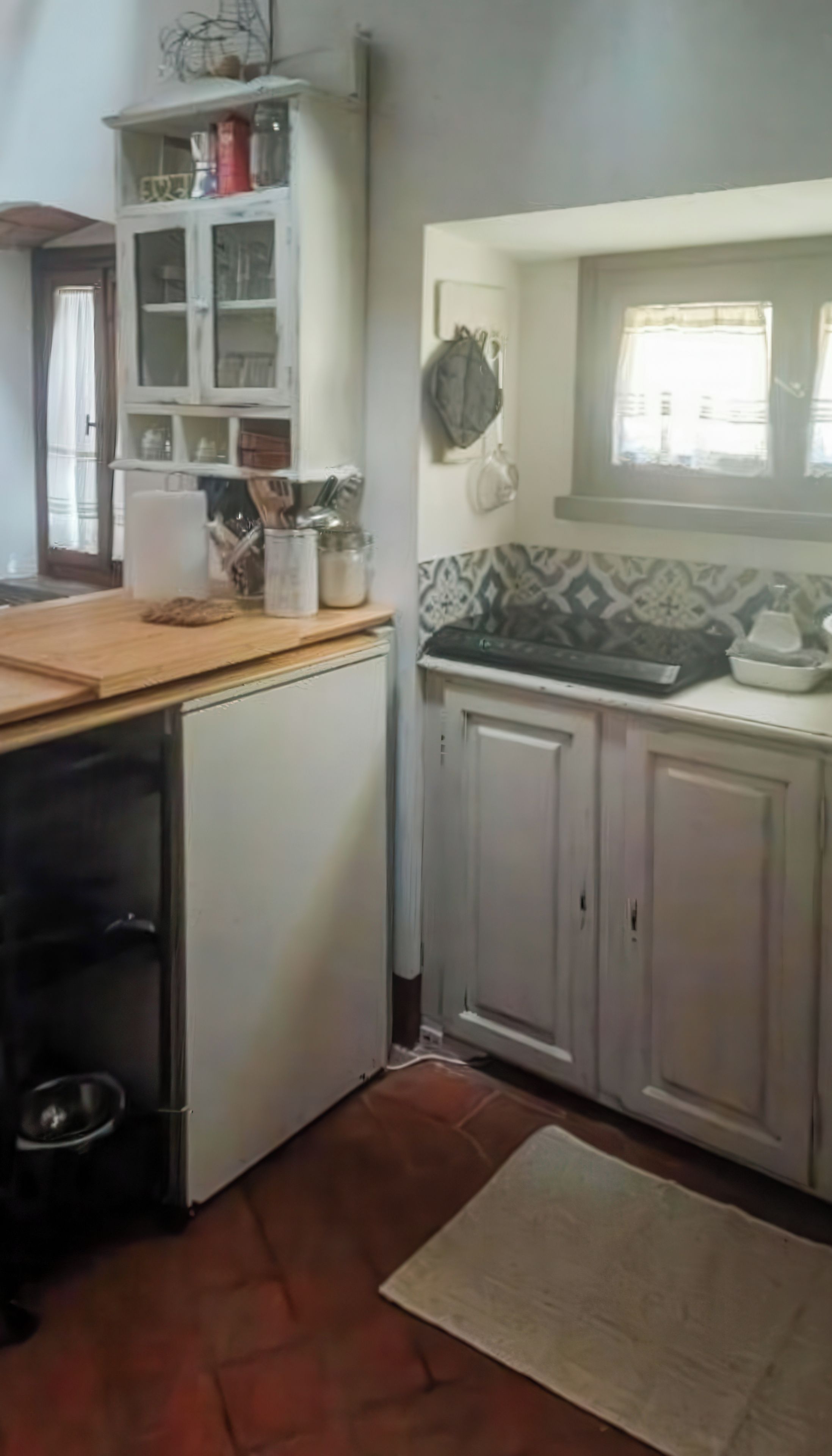 Une cuisine avec des meubles blancs, un plan de travail en bois et une fenêtre avec un rideau.
