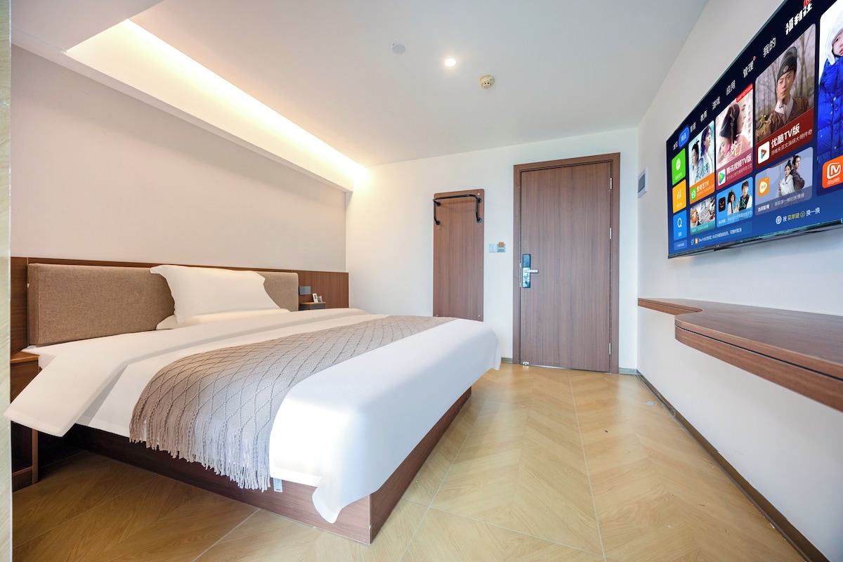 Een moderne hotelkamer met een groot bed, een flatscreen televisie aan de muur en een houten deur.