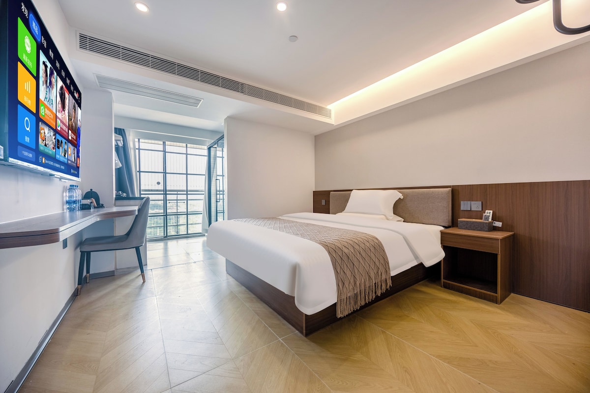 Een moderne hotelkamer met een groot bed, een bureau en een televisie waarop verschillende zenders te zien zijn.