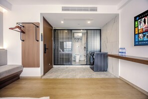 Een hotelkamer met een houten vloer, een grijze bank, een houten deur, een glazen scheidingswand, een wasmachine en een waterdispenser.