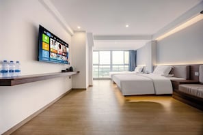 Moderni hotellihuone, jossa on suuri, seinälle asennettu litteänäyttöinen televisio, puulattia, valkoisilla tekstiileillä varustettu sänky, sohva ja ikkuna, josta avautuu näkymä kaupunkiin.