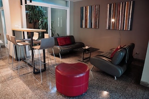 A modern living room with a sofa, ottoman, and chairs. There is a dining table with chairs, a coffee table, and artwork on the walls.
