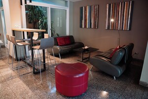 Una sala de estar moderna con un sofá, un reposapiés y sillones. Hay una mesa de comedor con sillas, una mesa de centro y obras de arte en las paredes.