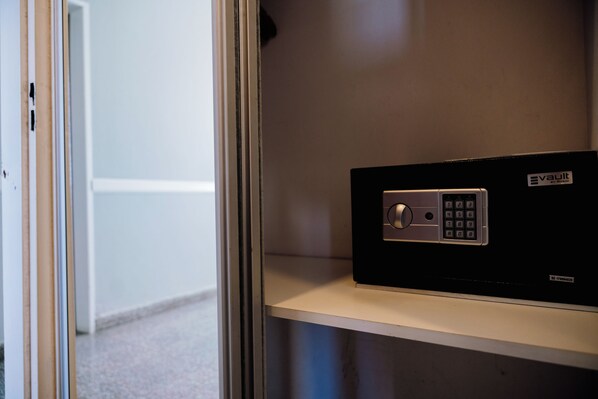 A secure vault with a keypad lock, located on a shelf in a room with a plain wall and a door in the background.