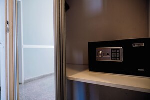 Una caja fuerte segura con cerradura numérica, ubicada en un estante en una habitación con pared lisa y una puerta al fondo.
