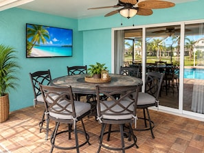 A covered patio with a round table and chairs, a ceiling fan, and a view of a swimming pool through glass doors. - Villa Serenity by swflorida-villas in Cape Coral (Cape Coral)