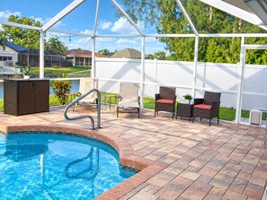 A covered outdoor swimming pool area with a patio, chairs, and a small table. - Villa Serenity by swflorida-villas in Cape Coral (Cape Coral)