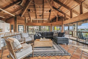 A spacious indoor area with a high ceiling, wooden beams, a large sofa, chairs, and a dining area with a view of the outdoors. - Private Island Oasis | Pool + Dock • Boat-In Only (Longboat Key)