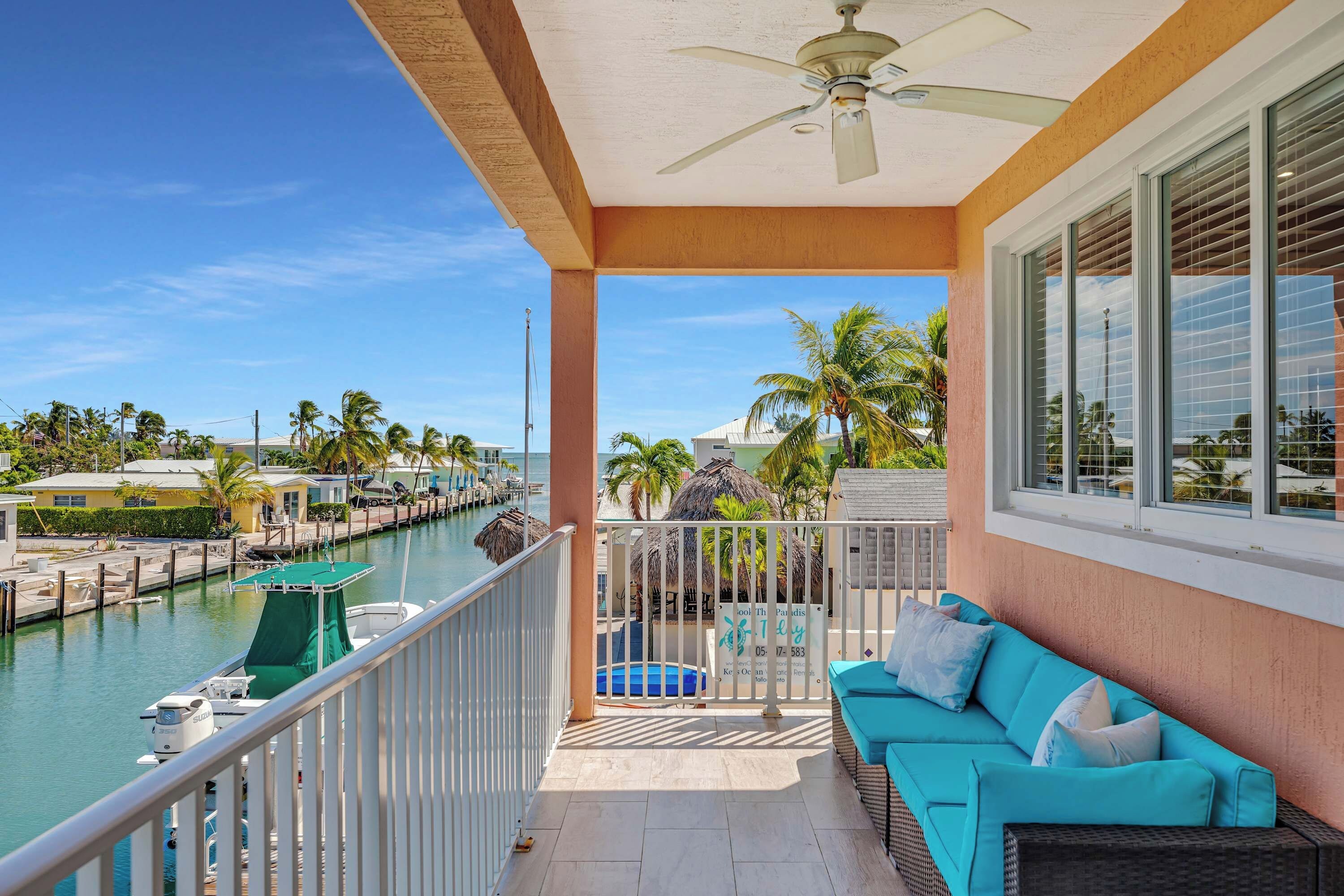 A balcony with a view of a marina, a pool, and a lounge area with cushions.