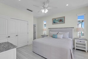 A bedroom with a bed, nightstands, a ceiling fan, and a painting. - Coral Tides - Waterfront Escape with 40' Dock (Marathon)