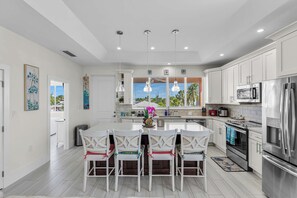 A modern kitchen with white cabinetry, stainless steel appliances, and a central island with chairs. - Coral Tides - Waterfront Escape with 40' Dock (Marathon)