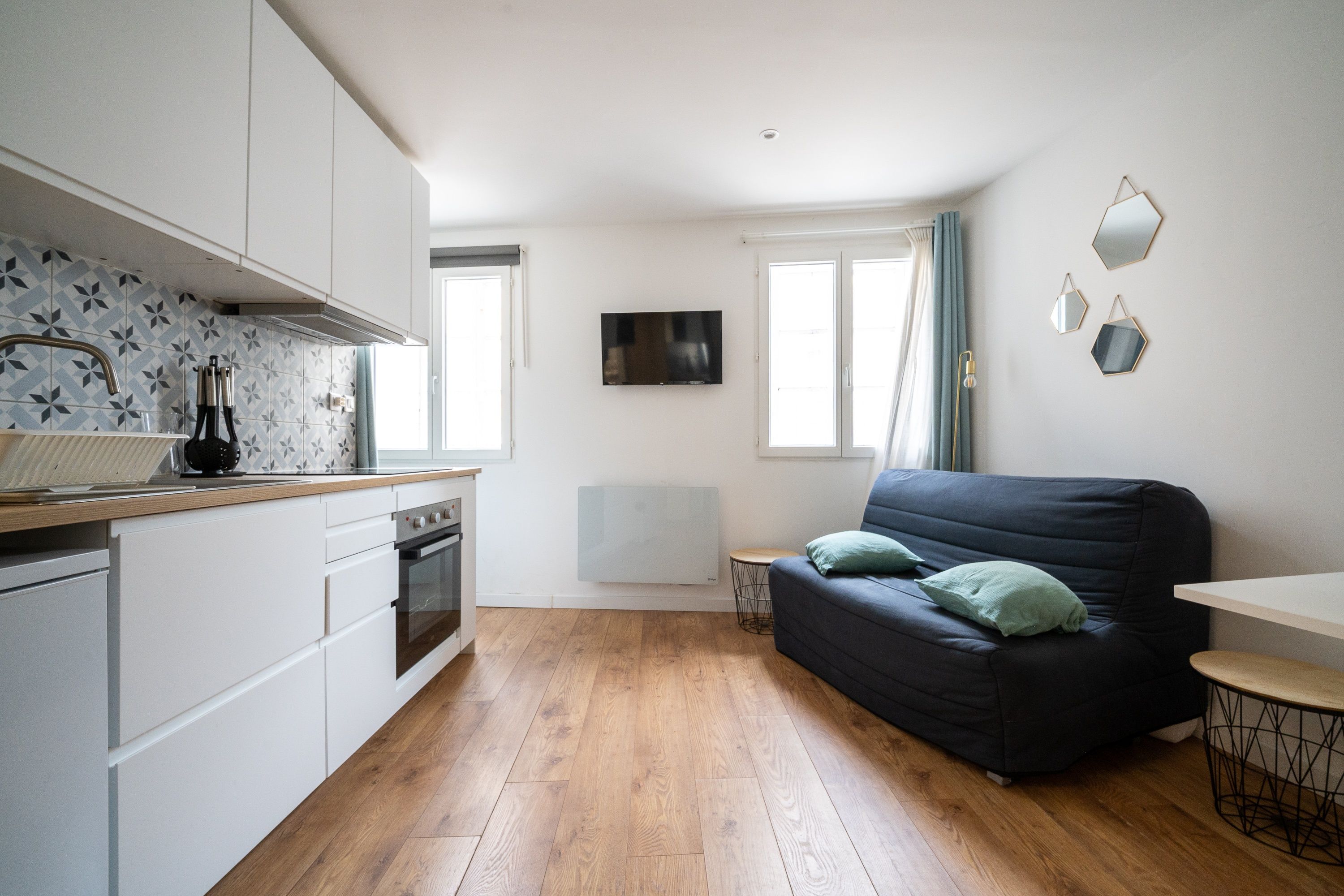 A compact living space with a kitchenette, a sofa, and a TV mounted on the wall.