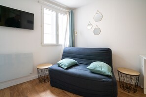A modern living room with a dark blue sofa, two round side tables, a flat-screen TV mounted on the wall, and a window with curtains. - L’Écrin d’Ax - 500 mètres des télécabines (Ax-les-Thermes)