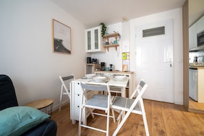 A compact kitchen with white cabinets, a dining table with chairs, and a small seating area with a couch and pillows. - L’Écrin d’Ax - 500 mètres des télécabines (Ax-les-Thermes)