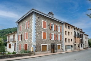A multi-story building with stone facade and red shutters, featuring a ground-level entrance and a visible sign. - L’Écrin d’Ax - 500 mètres des télécabines (Ax-les-Thermes)
