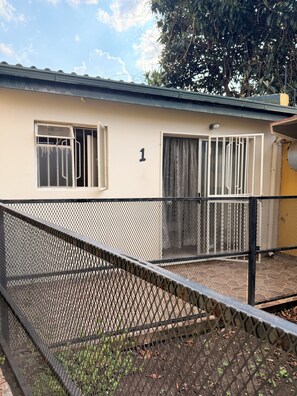 A building with a number '1' on the wall, a barred window, and a fenced outdoor area. - Charming humble cottage Johannesburg 4 min from Eastgate and very peaceful (Johannesburg)