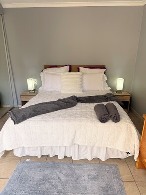 A neatly made bed with a white duvet, two pillows, and a grey blanket. There are two bedside lamps on wooden nightstands. - Charming humble cottage Johannesburg 4 min from Eastgate and very peaceful (Johannesburg)