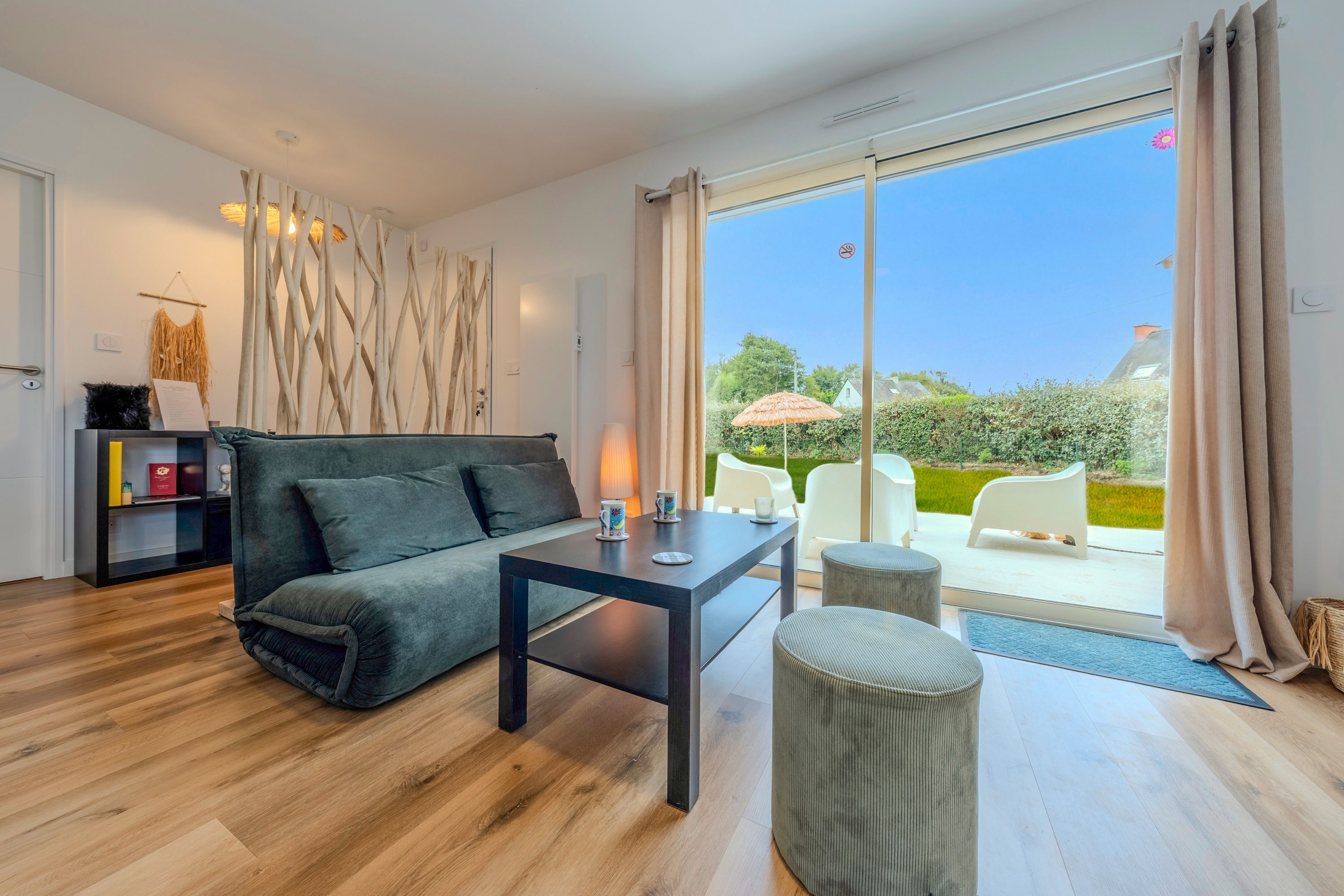 A modern living room with a sofa, a coffee table, and a view of a garden through large glass doors.