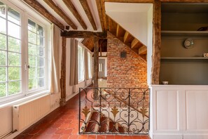 A room with exposed wooden beams, a brick wall, and a tiled floor. - Le Charme et le Chevreuil - Maison Normande (Rosay)