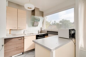 A modern kitchen with a large window, a built-in oven, and a countertop with a kettle. - Le Prestige du 16 - Proche de la Gare (Nancy)