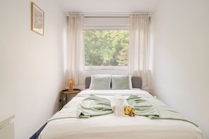 A neatly made bed with a green blanket, a bedside table with a lamp, and a window with curtains. - Le Prestige du 16 - Proche de la Gare (Nancy)