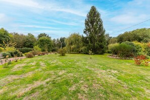 A well-maintained grassy lawn with a variety of trees and shrubs, a clear sky, and a stone wall in the background. - Le Cottage de Saint Cyr - Maison avec grand jardin (Saint-Pierre-de-Salerne)