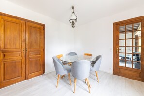 A dining area with a round glass table surrounded by four grey upholstered chairs with wooden legs. - Le Cottage de Saint Cyr - Maison avec grand jardin (Saint-Pierre-de-Salerne)