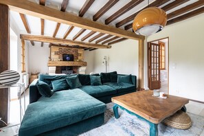 A cozy living room with a sectional sofa, a wooden coffee table, and a brick fireplace. - Le Cottage de Saint Cyr - Maison avec grand jardin (Saint-Pierre-de-Salerne)