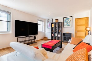 Ein modernes Wohnzimmer mit Fernseher, Bücherregal, Sofa und Couchtisch.