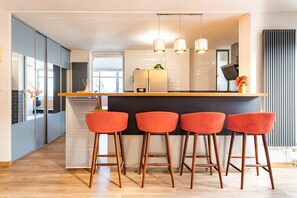 A modern kitchen with a central island, bar stools, pendant lighting, and a view into the adjacent dining area. - My Babylone - Climatisé avec parking privé (Toulouse)