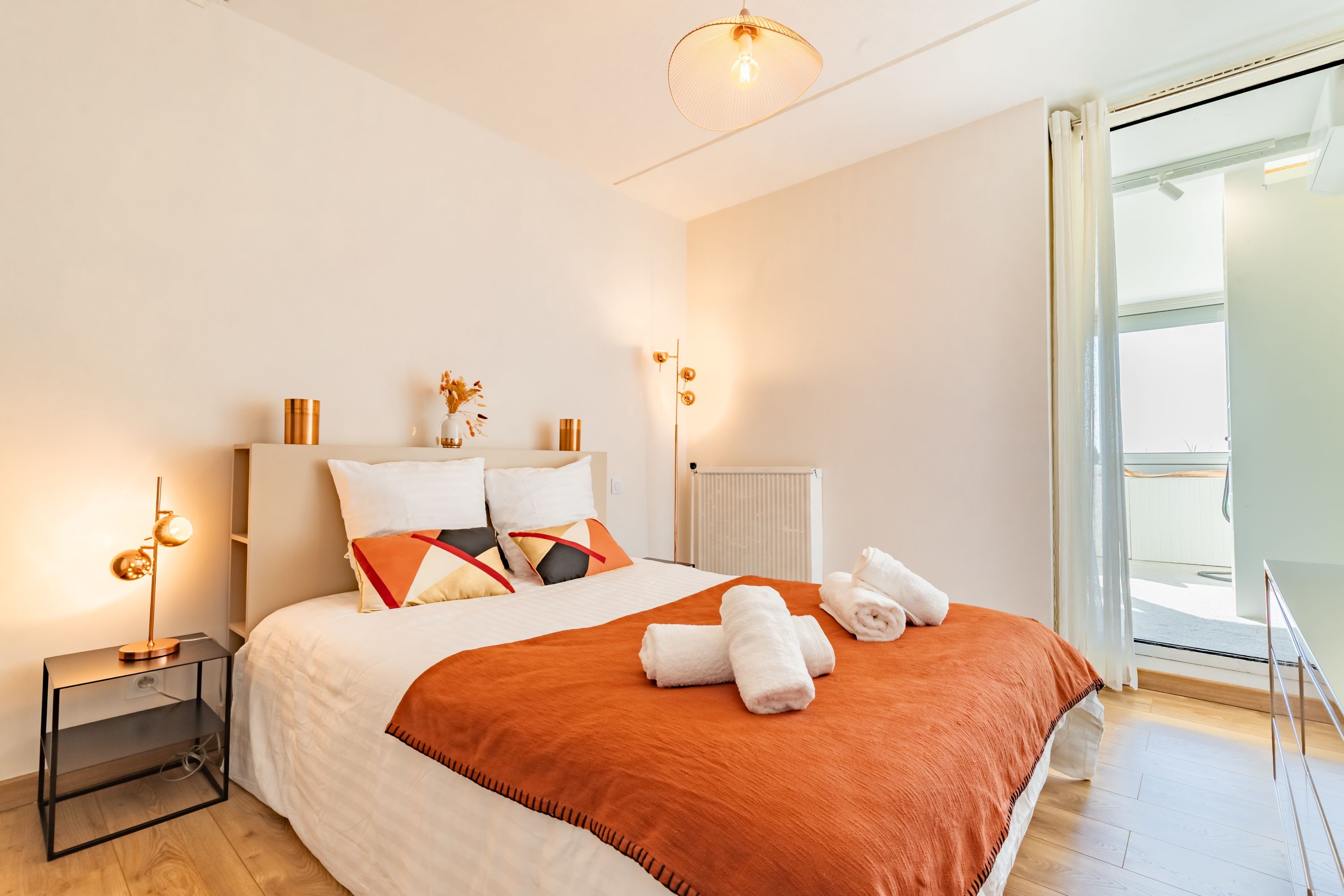 A modern hotel room with a large bed, a bedside table, a radiator, and a view of the outdoors.