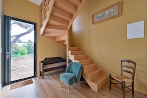 A modern interior with a wooden staircase, a blue chair, a wooden bench, and a painting on the wall. - La Maison du Logeo - A 300 m du Golfe (Sarzeau)