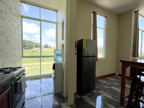 A kitchen with a gas stove, a refrigerator, a water dispenser, and large windows offering a view of the outdoors. - Brand-New Modern 2BR Apt at San Ignacio, Belize (San Ignacio)