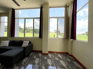 A room with a dark-colored sofa, a ceiling fan, and large windows with curtains. - Brand-New Modern 2BR Apt at San Ignacio, Belize (San Ignacio)