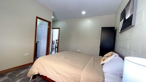 Ein Schlafzimmer mit einem Bett, einem Nachttisch, einer Lampe, einer Tür und einem an der Wand montierten Fernseher.