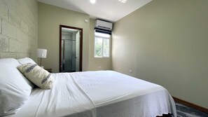 A hotel room with a bed, a window, an air conditioning unit, and a door leading to a bathroom. - New 2BR - 2BA Apartment at San Ignacio, Cayo (San Ignacio)