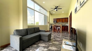 A living room with a sectional sofa, a dining area with a table and chairs, a kitchen with wooden cabinets, and a ceiling fan. - New 2BR - 2BA Apartment at San Ignacio, Cayo (San Ignacio)