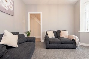 Ein Wohnzimmer mit zwei grauen Sofas, einem kleinen Topfpflanzen und einer weißen Tür, die zu einer Treppe führt.