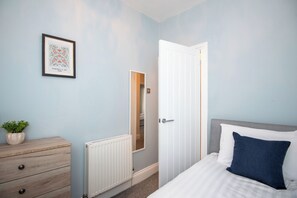 Ein Schlafzimmer mit einem Bett, einem Schminktisch, einem Heizkörper, einer Tür und einem gerahmten Bild an der Wand.