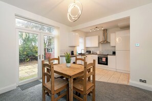 A modern kitchen with white cabinets, a dining table with chairs, and a large window. - Toast Stays - Teal View House (Darlington)