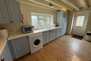 A kitchen with a washing machine, a microwave, and a window. - Toast Stays - Woodbine Cottage (Alston Moor)