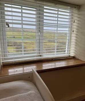 A room with a window with horizontal blinds, a wooden floor, and a white wall. - Toast Stays - Woodbine Cottage (Alston Moor)