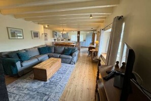 A spacious living room with a sectional sofa, a wooden coffee table, and a television. - Toast Stays - Woodbine Cottage (Alston Moor)