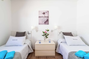 A hotel room with two single beds, a bedside table with a vase of flowers, and a wall-mounted picture. - Blue Beach - Three Bedroom Villa, Sleeps 6 (Tías)