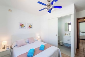 Ein Hotelzimmer mit Bett, Nachttischen, Deckenventilator und einem durch eine offene Tür einsehbaren Badezimmer.