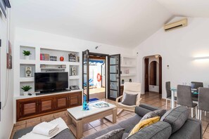 Ein modernes Wohnzimmer mit Fernseher, Couch, Esstisch und Stühlen.