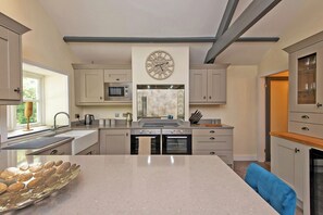 A modern kitchen with a central island, stainless steel appliances, and a clock on the wall. - Toast Stays - East Farm Cottage (Thinford)