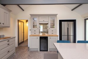 A modern kitchen with a built-in dishwasher, a refrigerator, and a dining area with a table and chairs. - Toast Stays - East Farm Cottage (Thinford)
