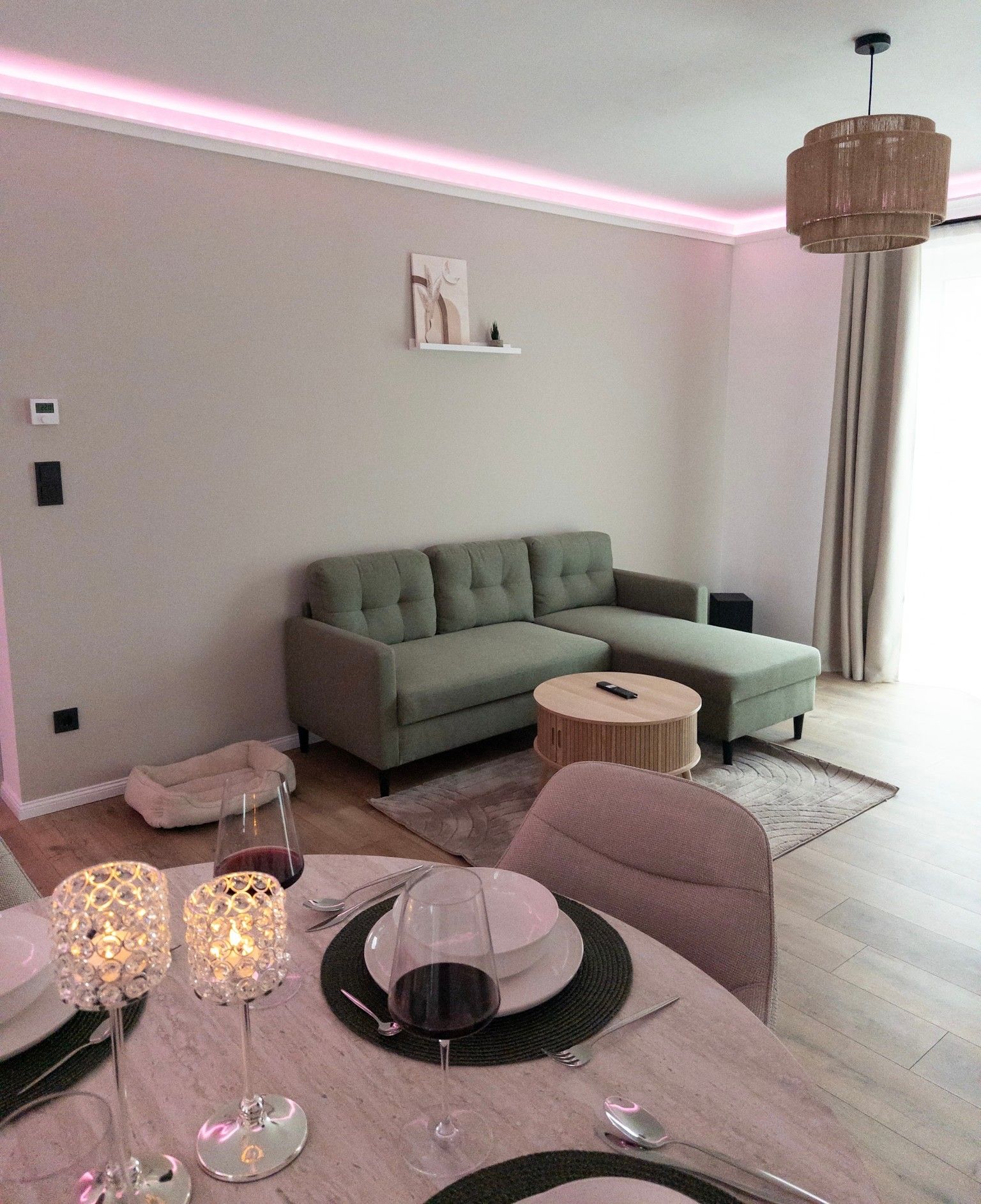 Una sala de estar moderna con un sofá seccional, una mesa de centro redonda y un comedor con una mesa, sillas y lámparas con velas.